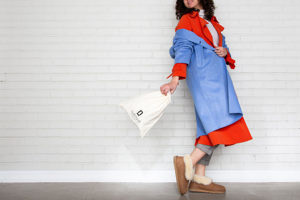 Woman wearing slippers facing wall with Nuknuuk logos on travel bag