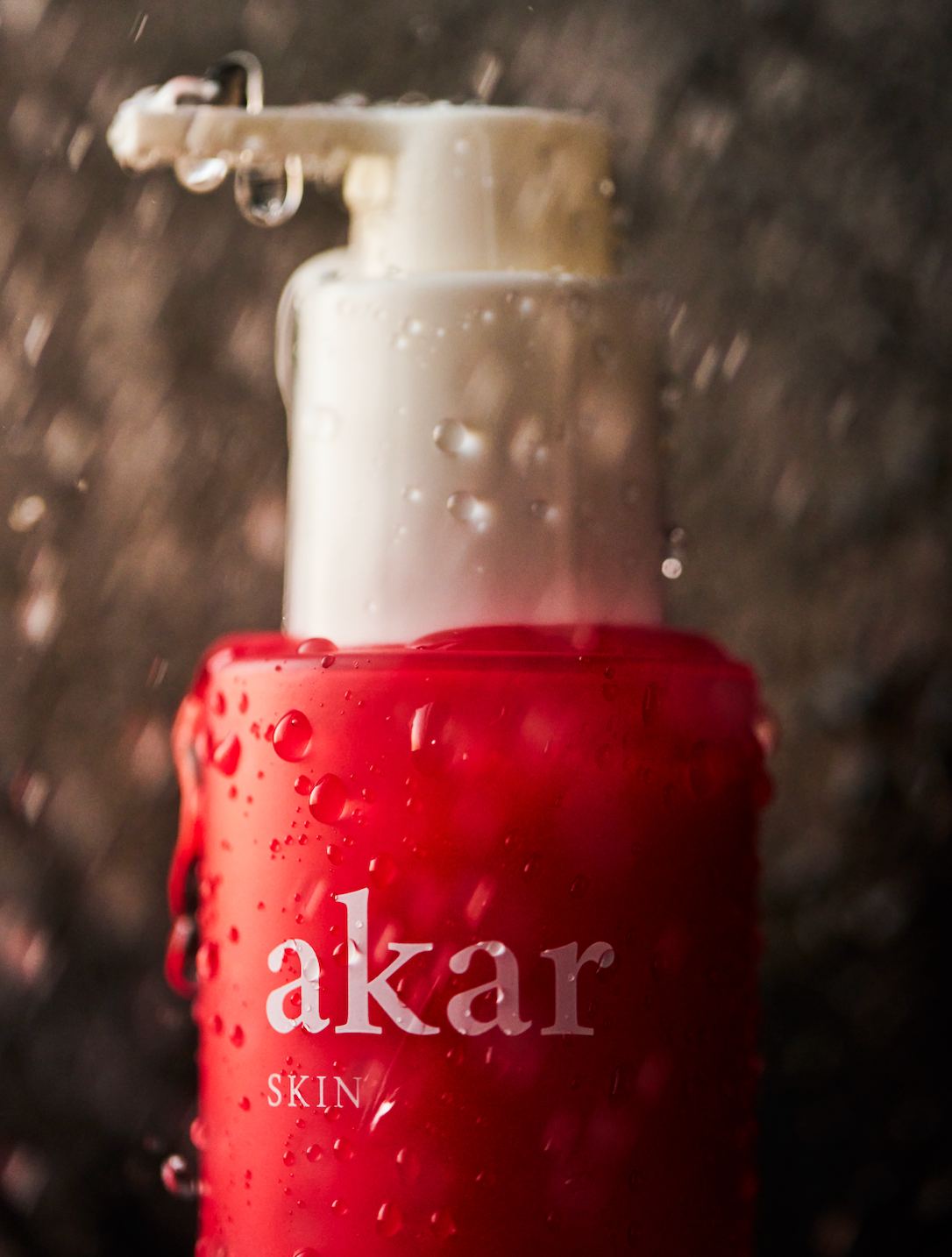 Close-up of a red Akar skin product bottle with water droplets.