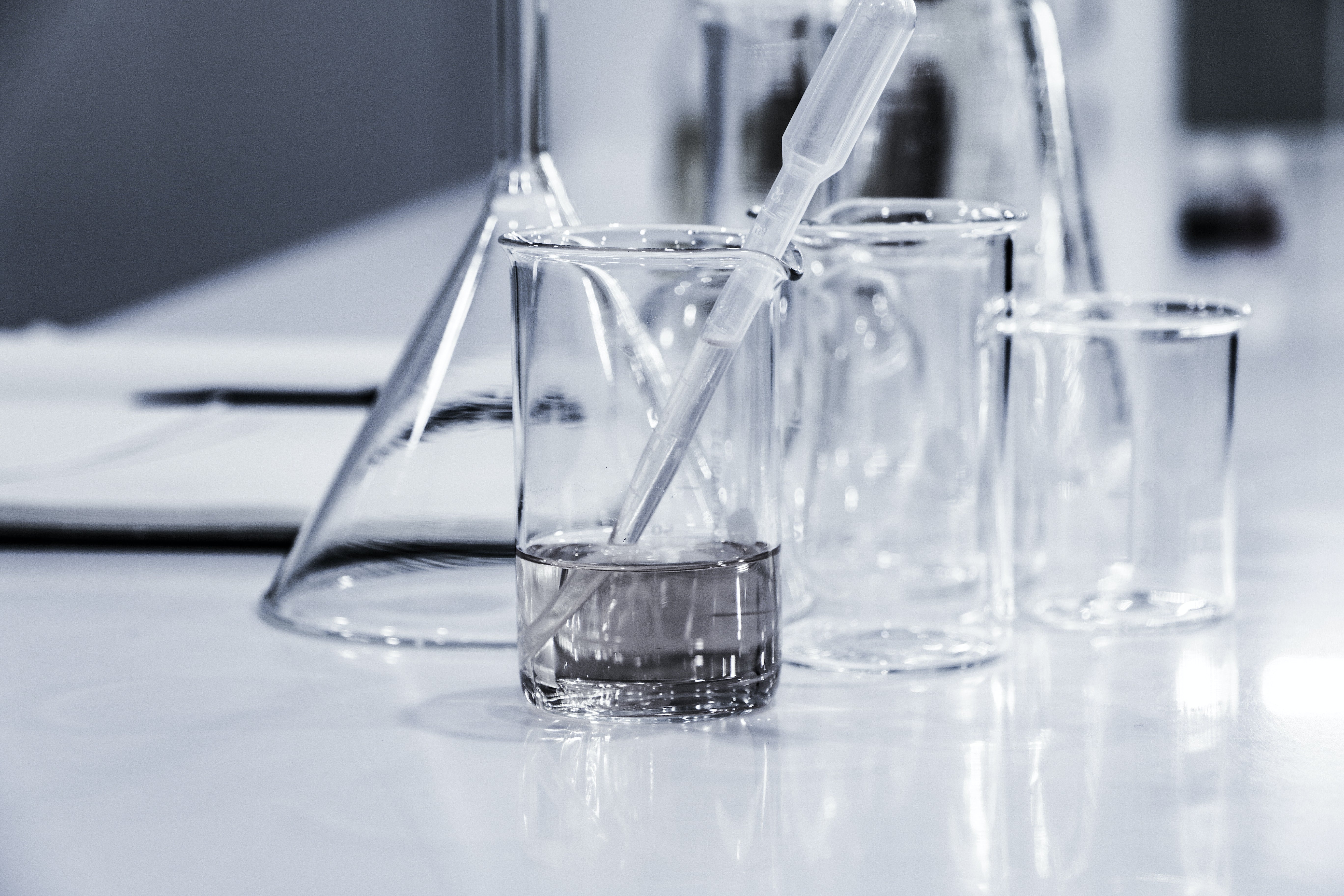 Photograph of a plastic pipette in a glass beaker filled with water, with empty glass beakers and a glass funnel in the background