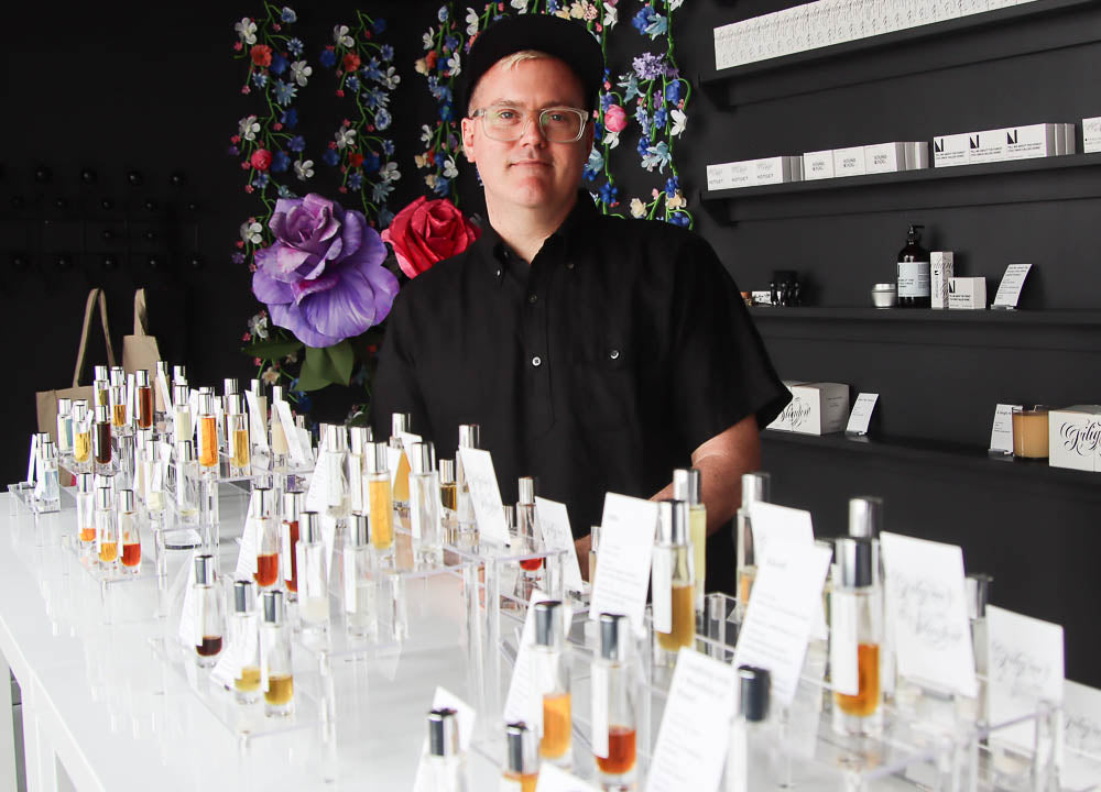 Perfumer James Elliott in his fragrance studio standing behind a white display table of his fragrances