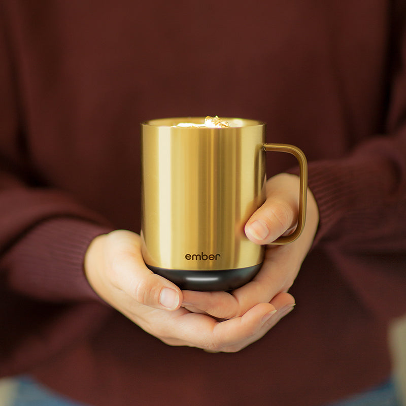 Person wearing a red sweater holding a gold Ember Mug with both hands.