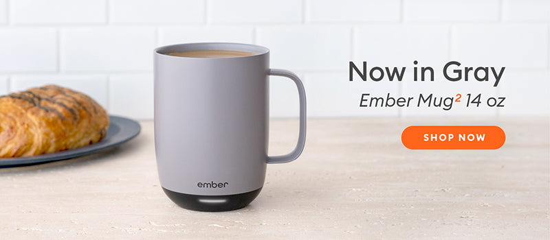 Ember Mug² 14 oz in Gray on a light wood table with a pastry in the background.