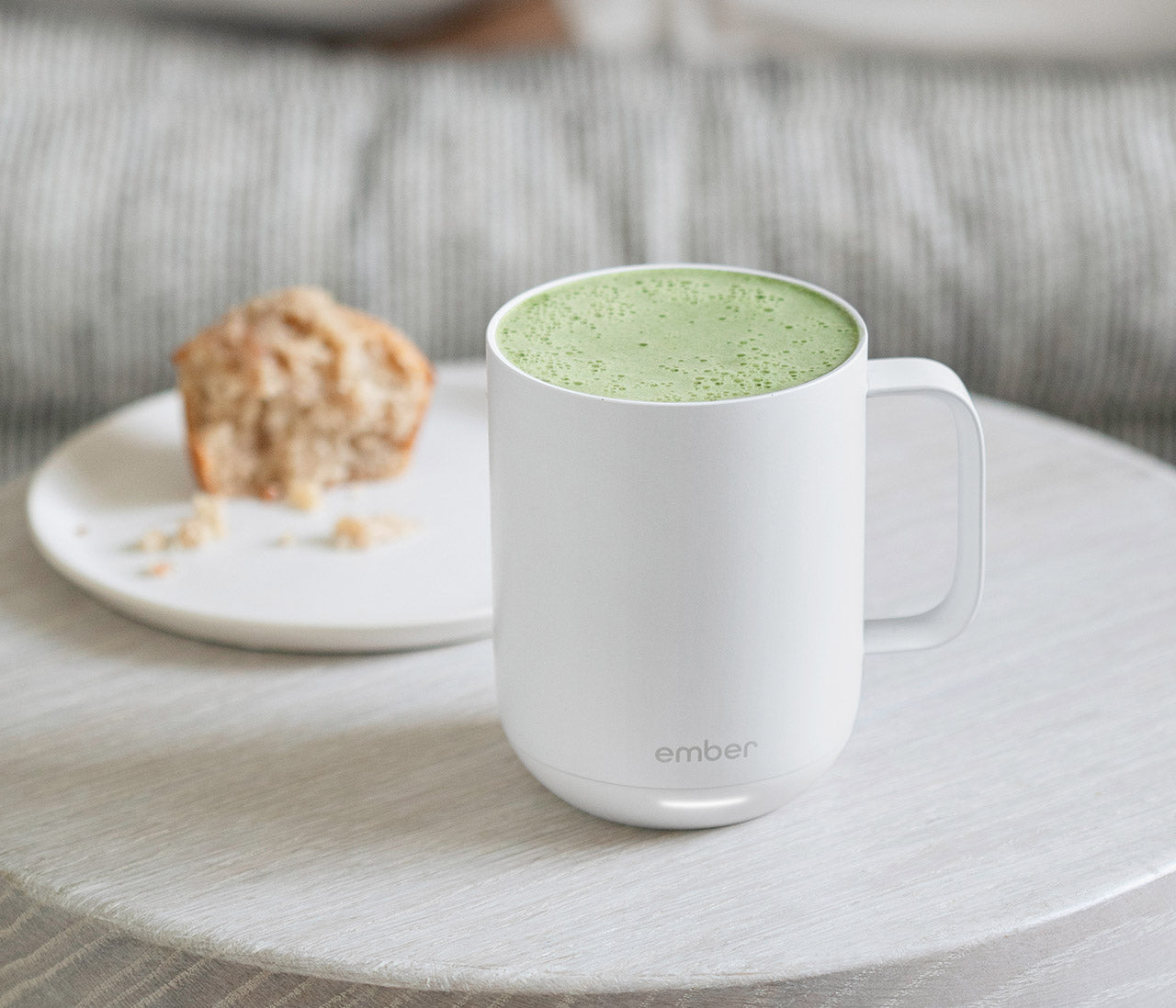 A frothy matcha latte sitting next to a crumbly muffin.