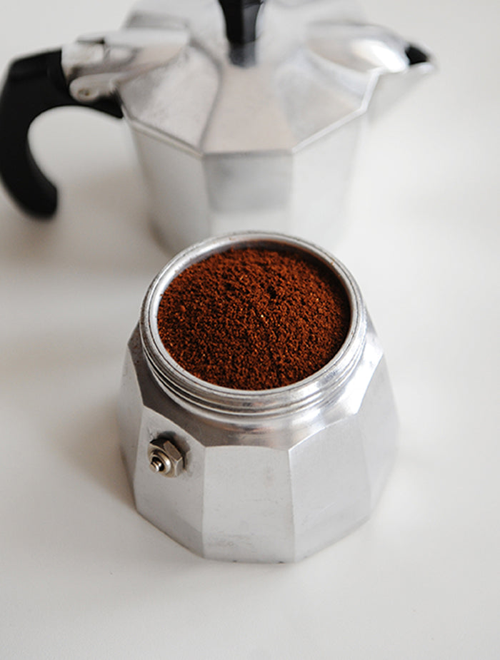 Fine coffee grounds sit neatly inside the bottom chamber of a stainless steel moka pot.