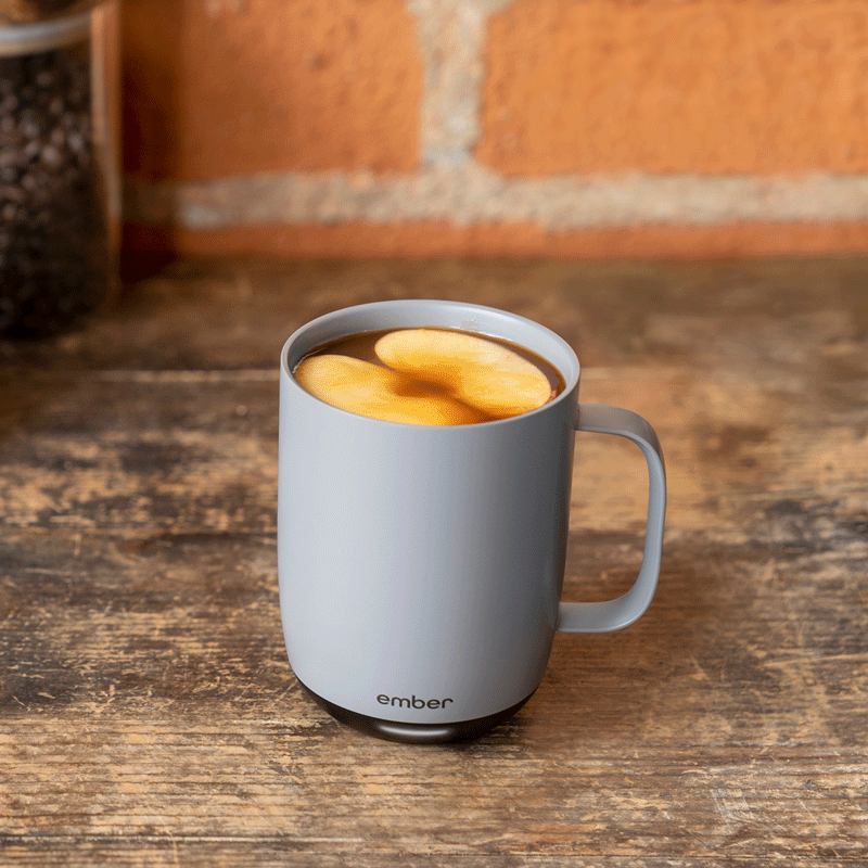A gif of a gray Ember Mug shows the mug filled with coffee and apples, then topped with whipped cream, and finally added a caramel drizzle.