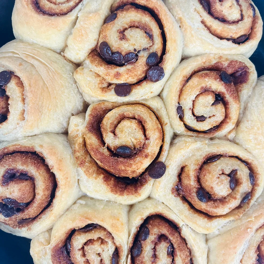 Close-up of freshly baked cinnamon rolls tightly arranged, topped with chocolate chips. Dough is golden-brown, creating a warm, inviting texture.