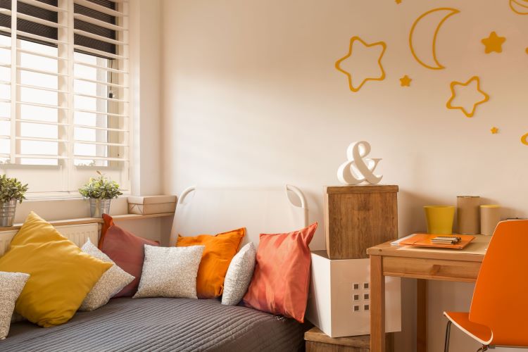 bedroom with many coloured cushions on a child bed, window with shutters and darkening blinds