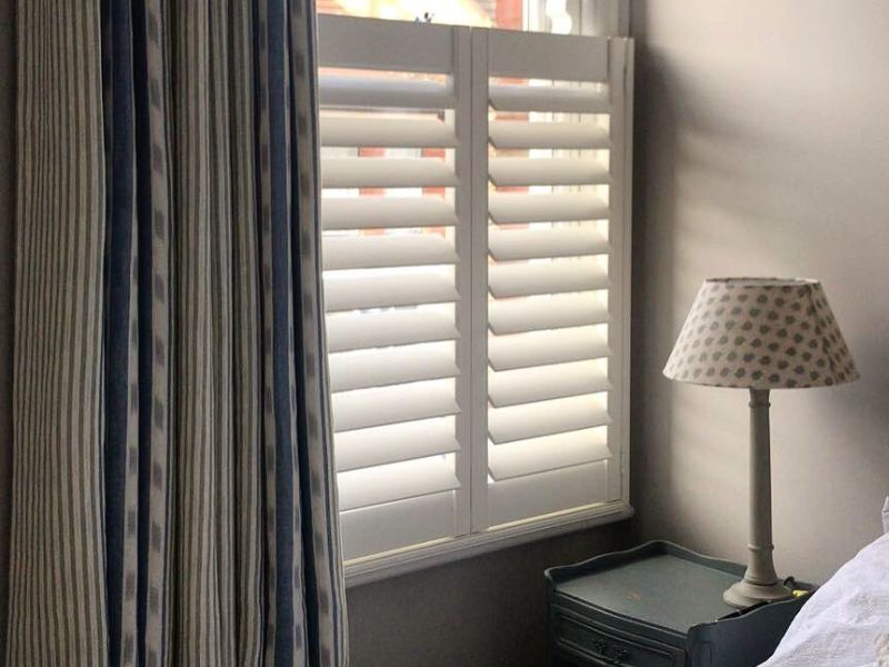 a bedroom with a shutters on the window and an open curtain