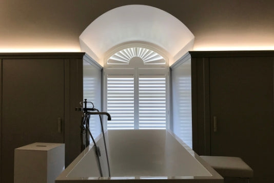 dark bathroom with modern bath tub and white shutters on the arched window