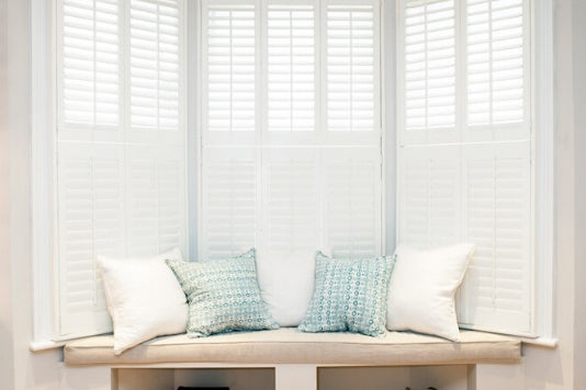 bay window with white shutters in tier on tier style with small bench and cushion in front