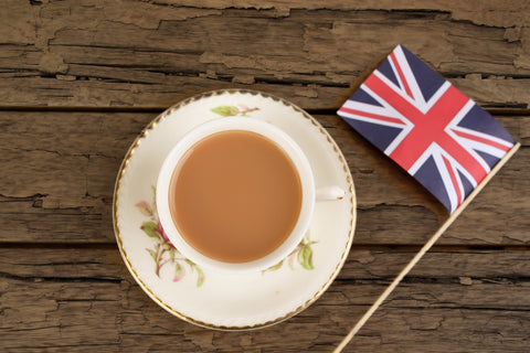 A Cup of Earl Grey Tea Mixed with Milk on a Saucer Next to a small replica of the British Flag