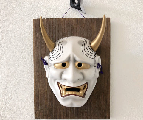 Japanese demon mask attached with wooden panel and hanging on the white wall.