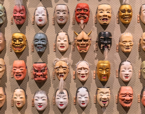 A bunch of Japanese Noh theater masks hanging in rows on a wall depicting various faces expressions