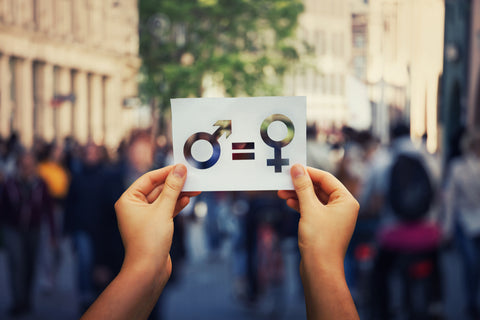 Gender equality concept as woman hands holding a white paper sheet with male and female symbol over a crowded city street background. Sex sign as a metaphor of social issue.