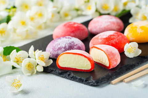 Multi-colored Japanese ice cream Mochi in rice dough and Jasmine flowers on a concrete blue background. Traditional Japanese dessert on a black slate