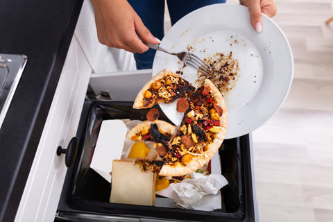 Close-up Of A Person Throwing Pepperoni Pizza On Plate In Dustbin