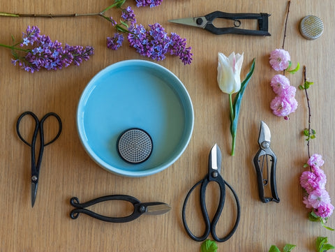 Tools for ikebana: hasami scissors, pruner shears, scissors, kenzene, a vase and flowers on a wooden table