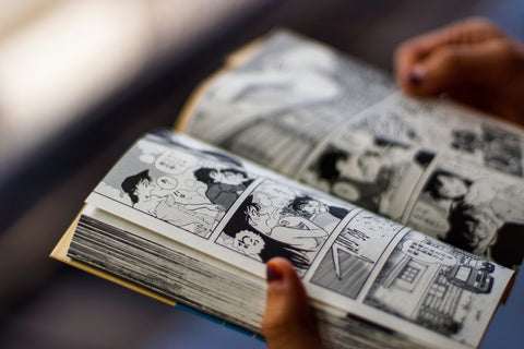 Close up of an adult person hands open and holding a Japanese comic book with bokeh background.