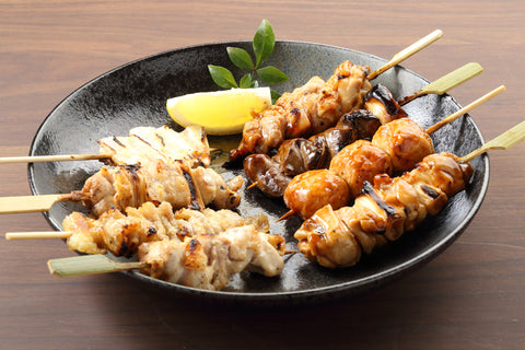 A plate serving eight meat skewers, or Japanese yakitori, beside a lemon wedge.