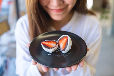 Closeup image of a young woman holding a plate of strawberry Mochi or Ichigo Daifuku, sweet red bean dessert