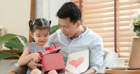 Happy Asian young father surprise with red gift box and heart colored greeting cards from daughter