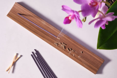 Overhead view of burning japanese incense stick on wooden holder and pink orchid flowers