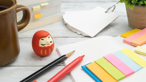 An image of studying for an exam. Stationery and Japanese Daruma dolls