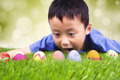 ortrait of surprised little boy lying on the grass and finding easter eggs, shot with blurred background