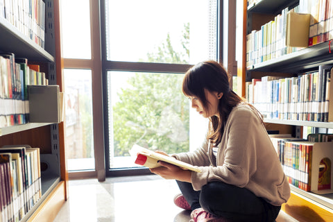 A girl sits reading a book on the floor of the library