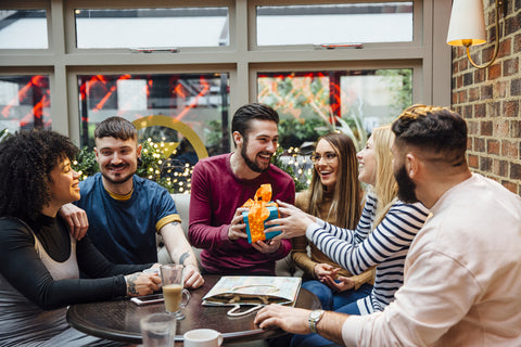 Friends are hanging out in a bar, celebrating one of the women's birthday. She is receiving a gift from one of the men at the table.