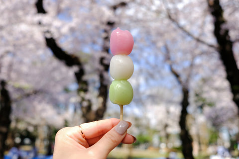 Person holding up hanami dango in front of sakura trees.