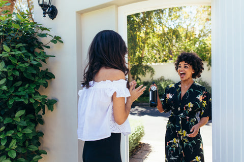 Woman giving a wine bottle her friends at entrance door.