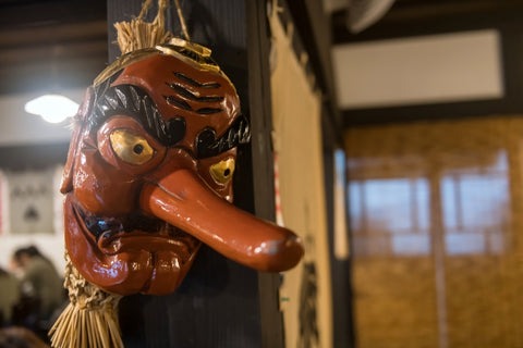 Red Japanese Tengu Mask hanging on wooden wall in Japanese building.