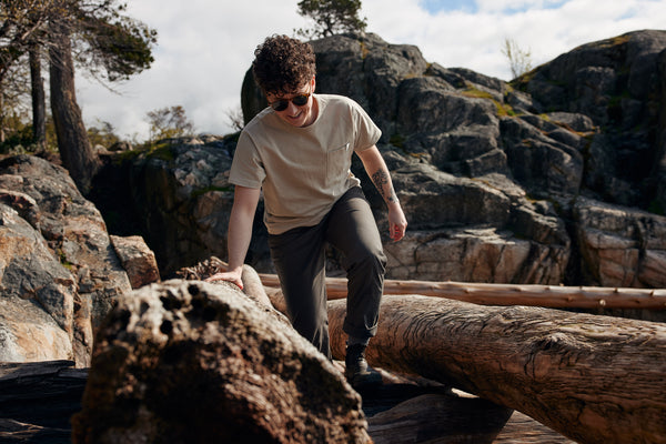 AK MacKellar steps over boulders and logs wearing the ecologyst Heavyweight Tee in Oyster and Park Pant in Ivy.