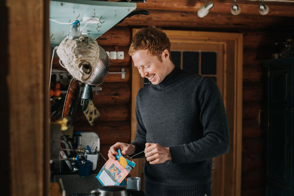 Joel Fuller scoops some coffee beans out of a bag to make coffee while wearing the Merino Turtleneck in his off-grid cabin.