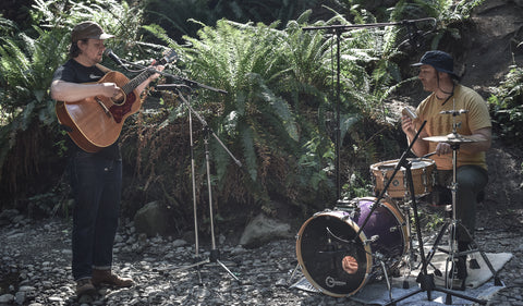 Jon and Roy musicians wearing ecologyst clothing and performing a song in forest and river setting