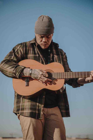 Logan Staats playing guitar in front of a blue sky wearing an ecologyst Wool Shirt in Plaid and a Merino/Cashmere Toque in Grey