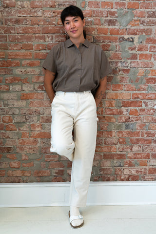 Robyn Jin stands against a brick wall wearing the Women's Cotton Canvas Pant in Salt and the Tencel Shirt in Mushroom