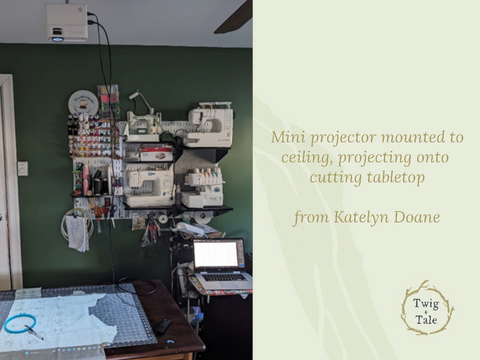 A mini projector setup by Katelyn Doane - the projector is mounted with a regular projector mount, and projecting down onto a tabletop. A laptop is connected via HDMI cord, and sewing machines and supplies are stored on a wall rack