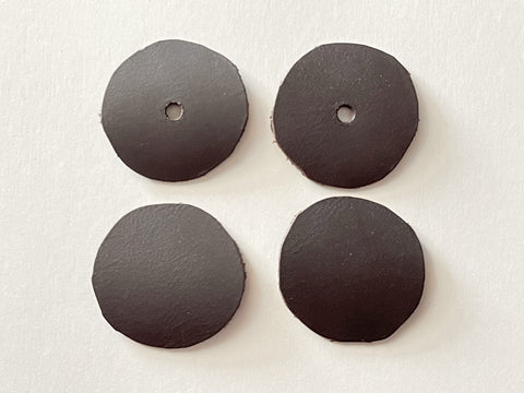 Four dark leather circles are shown laid flat - the top two have had a small hole punched in the center.