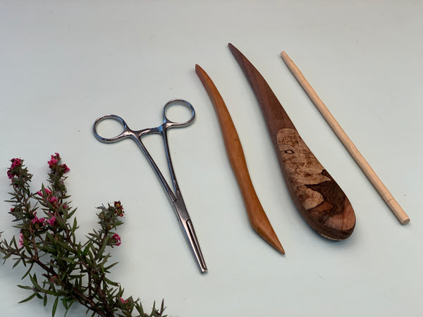 Various stuffing tools used to stuff woven dolls and toys. Haemostats, point turners, chopsticks, and a sculpting tool for clay. A small floral sprig of leaves sits to the left of the tools.