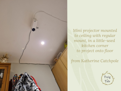 A projector setup by Katherine Catchpole - a mini projector is mounted to the ceiling with a regular projector mount, in a little-used kitchen corner. Cords are carefully anchored to the wall and ceiling to keep them out of the way, so that the projector can display the image on the floor for cutting.