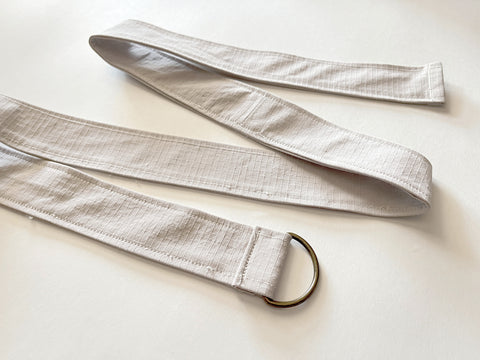 The raw end of the strap has been turned under and stitched down, to finish the edge and enclose the D-ring. The full length of the strap is shown laid in a zig-zag pattern.