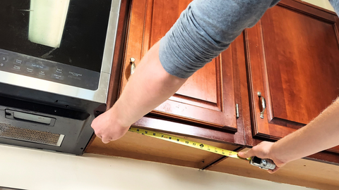 measuring underneath the cabinets with a tape measure