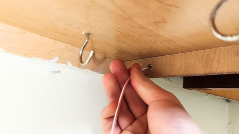 hand inserting wire though drilled hole in the cabinet joint