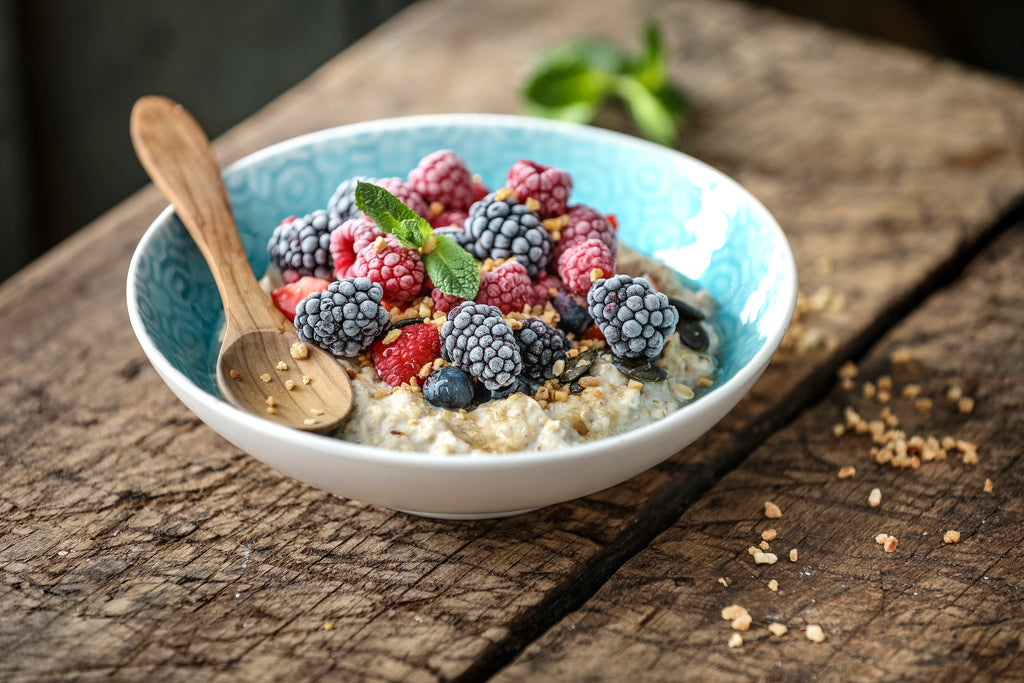 Porridge Bowl Holzlöffel Erdnüsse gefrorene Beeren Kürbiskerne Agavensirup