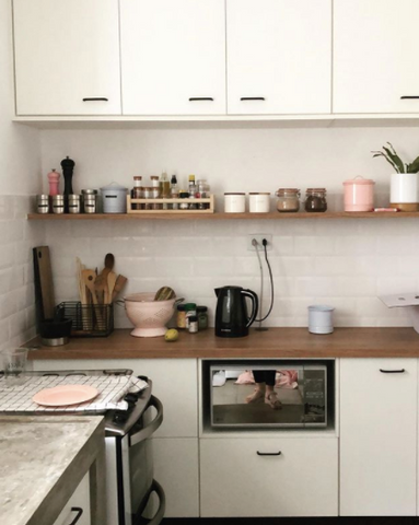 a imagem mostra uma cozinha com armários altos, prateleiras e um balcão. sobre ele temos alguns itens de cozinha, como um escorredor de macarrão e uma jarra de água