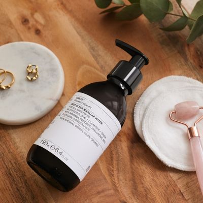 deep clean cleansing micellar water on wooden table with rose quartz face roller and gold jewellery