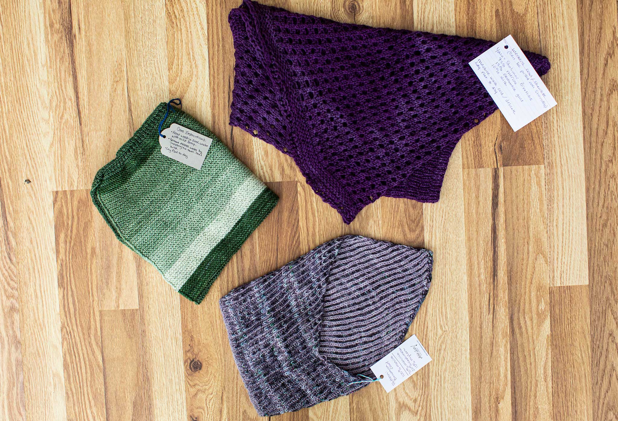 Various beautiful knitted shawls and cowls!  One in shades of green, one in a lustrous dark purple, and another in shades of grey with hints of subtle color within.