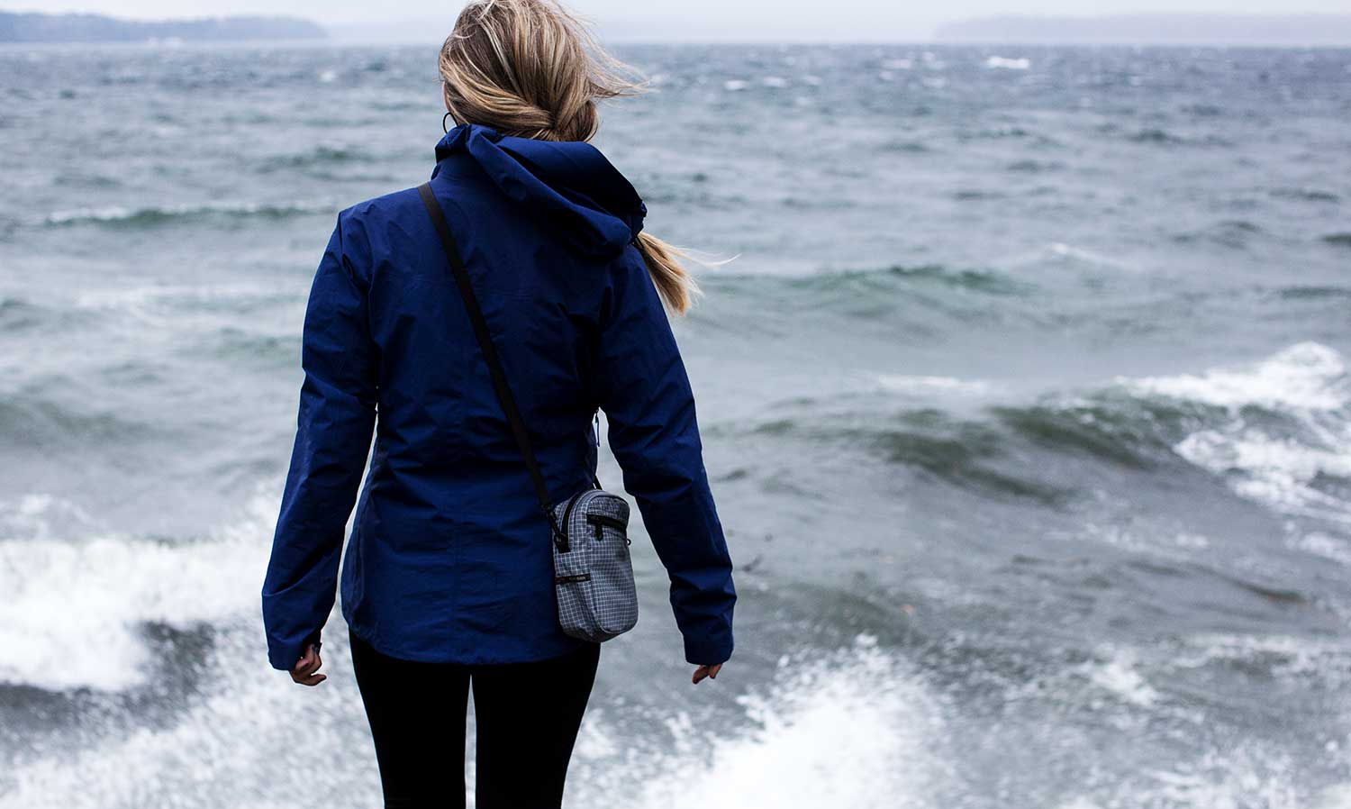 Person standing in front of the ocean on a stormy day wearing a raincoat and an Everyday Cubelet in Northwest Sky